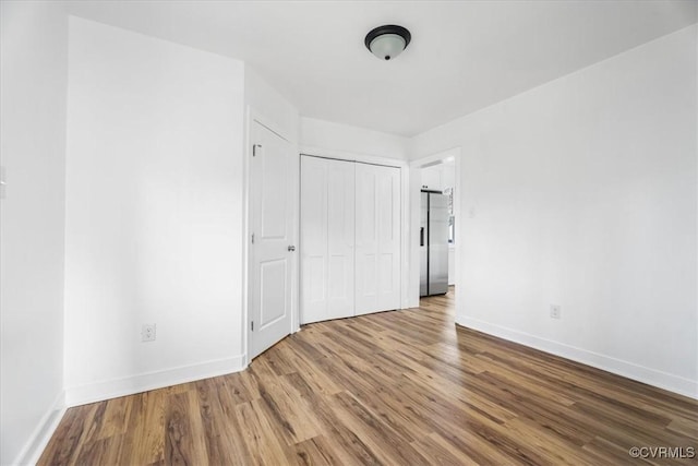 unfurnished bedroom with stainless steel fridge, a closet, baseboards, and wood finished floors