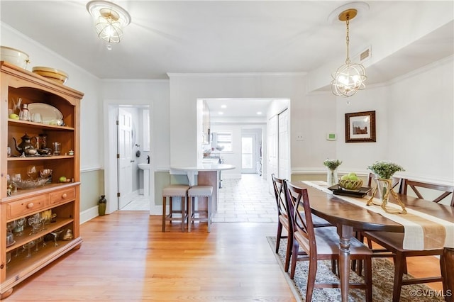 dining area featuring a chandelier, visible vents, crown molding, and light wood finished floors