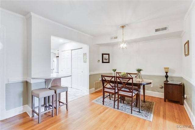 dining area featuring light wood-style floors, visible vents, ornamental molding, and baseboards