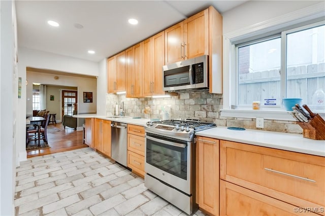 kitchen featuring light brown cabinets, stainless steel appliances, a sink, light countertops, and tasteful backsplash