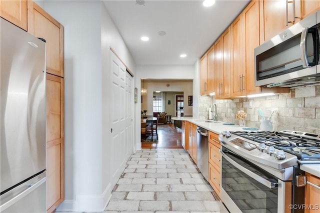 kitchen featuring decorative backsplash, stainless steel appliances, light countertops, light brown cabinetry, and a sink