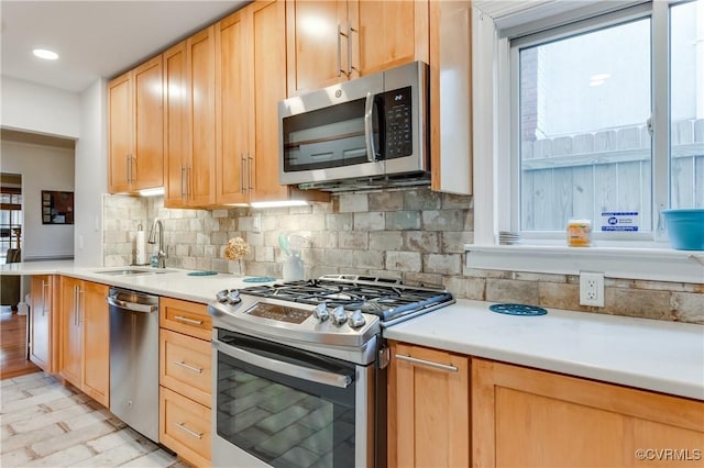 kitchen with light countertops, backsplash, light brown cabinetry, appliances with stainless steel finishes, and a sink