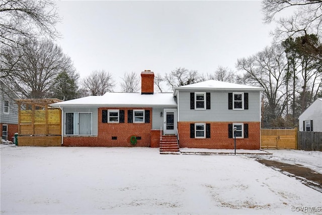 tri-level home with a chimney, fence, and brick siding