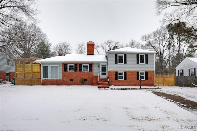 view of front facade featuring crawl space, brick siding, fence, and a chimney