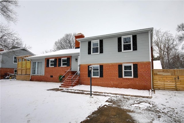 tri-level home featuring a chimney, fence, and brick siding