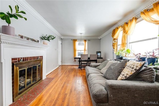 living area with ornamental molding, a brick fireplace, wood finished floors, and baseboards