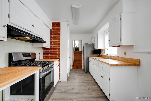 kitchen featuring appliances with stainless steel finishes, white cabinetry, a sink, light wood-type flooring, and under cabinet range hood