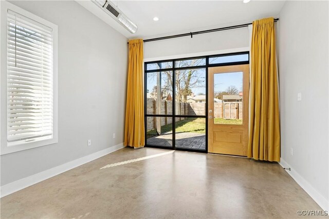 unfurnished room with finished concrete flooring, plenty of natural light, and baseboards