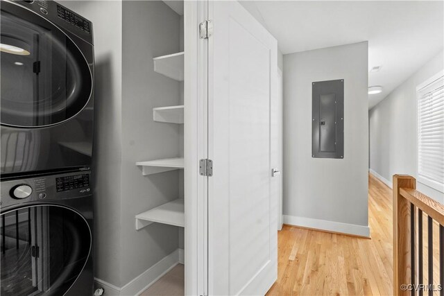 laundry area with laundry area, stacked washer / dryer, baseboards, electric panel, and light wood finished floors