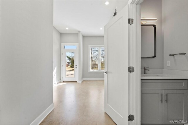 hall with finished concrete floors, baseboards, a sink, and recessed lighting