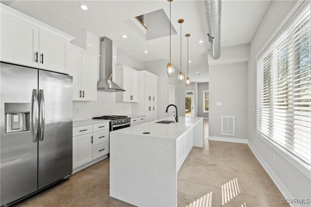 kitchen featuring a kitchen island with sink, light countertops, appliances with stainless steel finishes, hanging light fixtures, and wall chimney exhaust hood