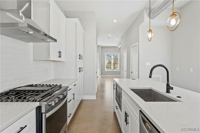 kitchen featuring wall chimney exhaust hood, appliances with stainless steel finishes, hanging light fixtures, light countertops, and a sink