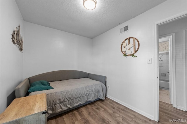 bedroom with baseboards, a textured ceiling, visible vents, and wood finished floors