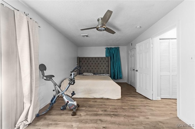 bedroom with a textured ceiling, wood finished floors, visible vents, and a ceiling fan