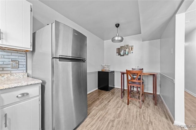 kitchen featuring light wood finished floors, white cabinets, freestanding refrigerator, light countertops, and pendant lighting