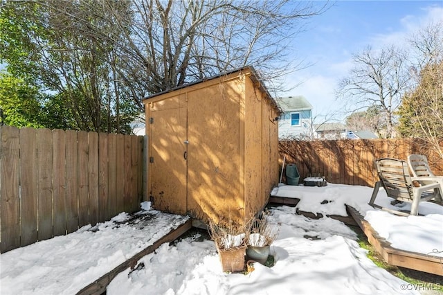 snow covered structure with a storage shed, a fenced backyard, and an outbuilding