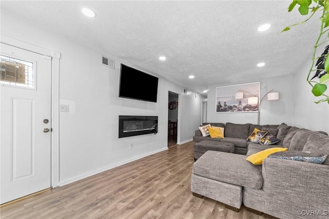 living area featuring a textured ceiling, recessed lighting, wood finished floors, visible vents, and a glass covered fireplace