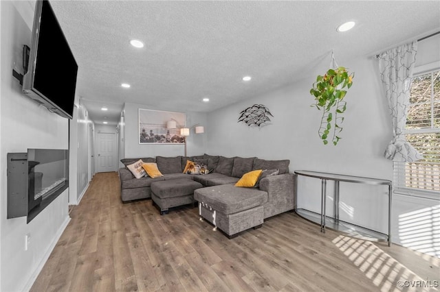 living area featuring recessed lighting, a glass covered fireplace, a textured ceiling, and wood finished floors