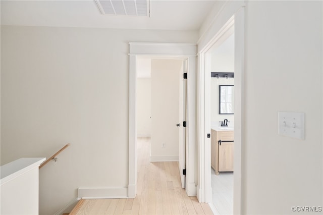 corridor with a sink, an upstairs landing, visible vents, baseboards, and light wood-type flooring