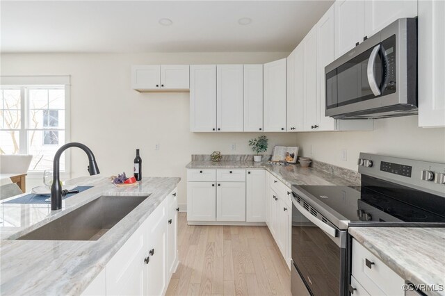 kitchen with white cabinets, light wood-style flooring, appliances with stainless steel finishes, light stone countertops, and a sink