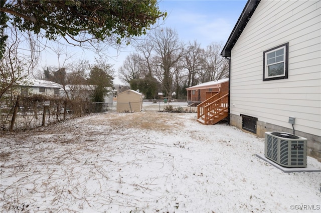 yard layered in snow with fence, a shed, an outdoor structure, and central AC unit