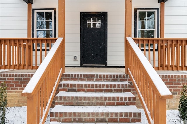 snow covered property entrance with covered porch and brick siding