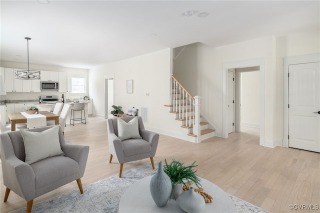 living area with stairs, light wood-type flooring, visible vents, and baseboards