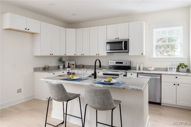 kitchen featuring stainless steel appliances, an island with sink, white cabinetry, and light wood-style floors