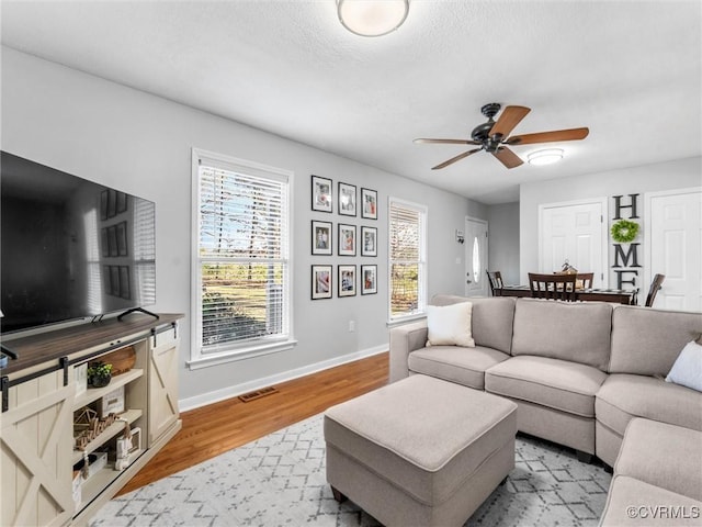 living room with a ceiling fan, visible vents, light wood-style flooring, and baseboards