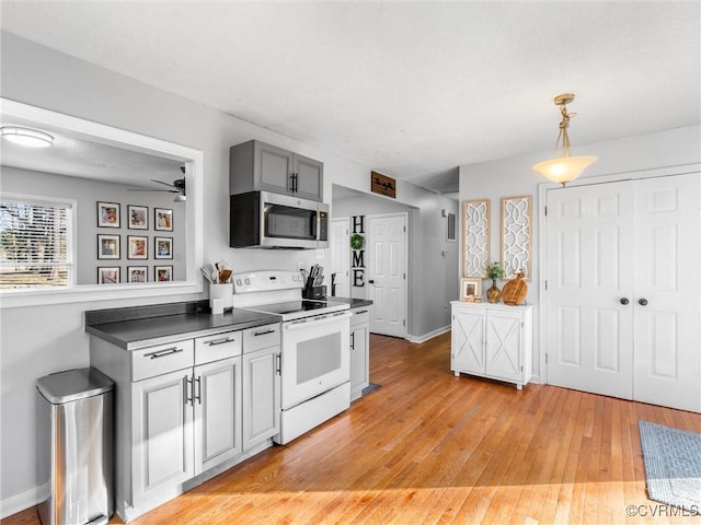 kitchen with white range with electric stovetop, pendant lighting, dark countertops, stainless steel microwave, and light wood-style flooring