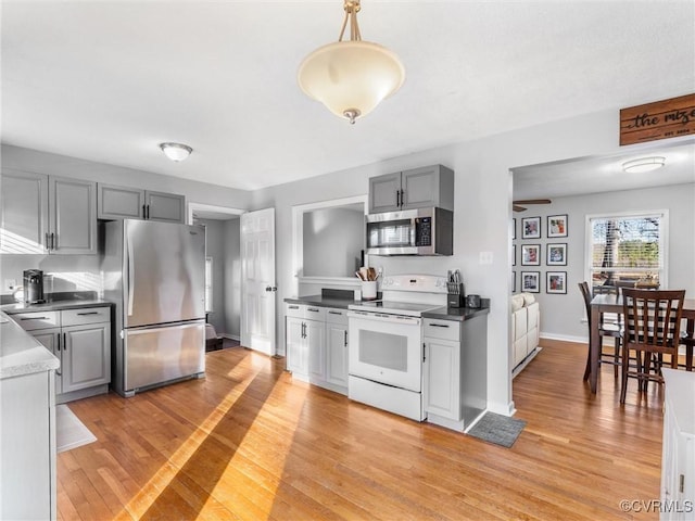 kitchen with appliances with stainless steel finishes, gray cabinets, pendant lighting, and light wood finished floors