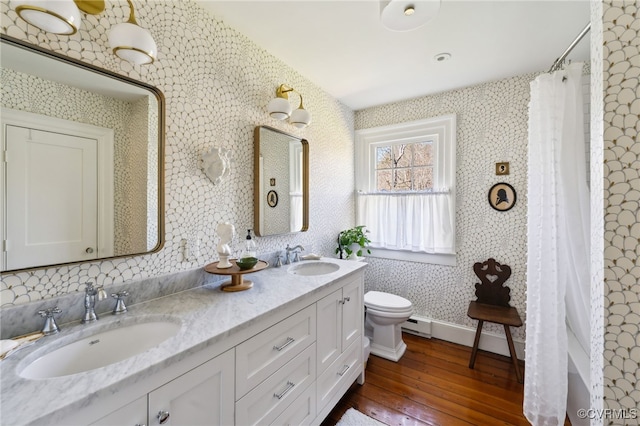 full bath with double vanity, wallpapered walls, a sink, and wood finished floors