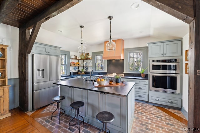 kitchen with brick floor, stainless steel appliances, dark countertops, a kitchen bar, and a center island with sink