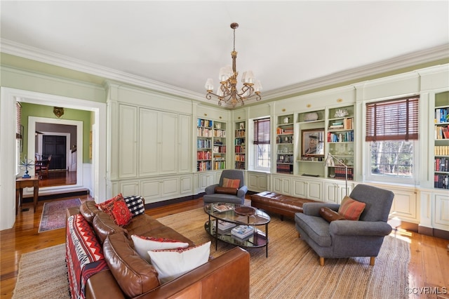 living room with built in shelves, a notable chandelier, wainscoting, light wood-type flooring, and crown molding