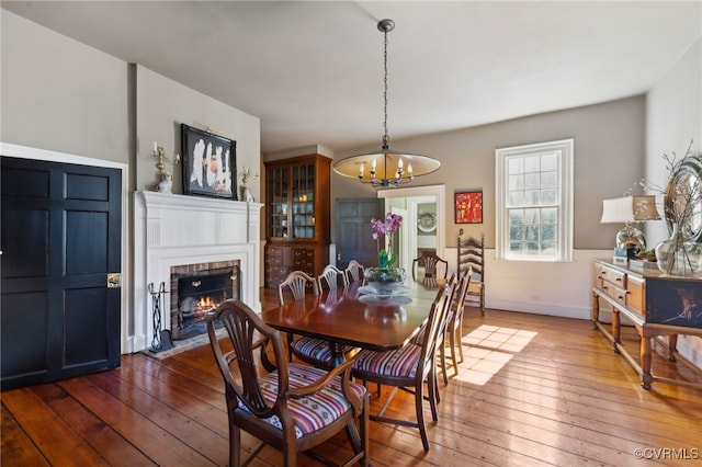 dining room with baseboards, dark wood-style flooring, a fireplace with flush hearth, and a notable chandelier