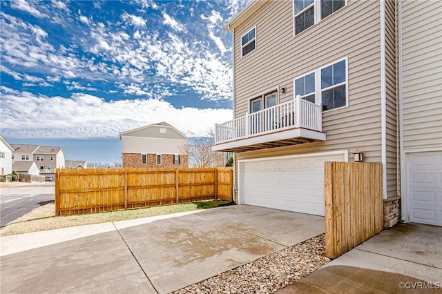 view of home's exterior featuring a garage, concrete driveway, fence, and a balcony