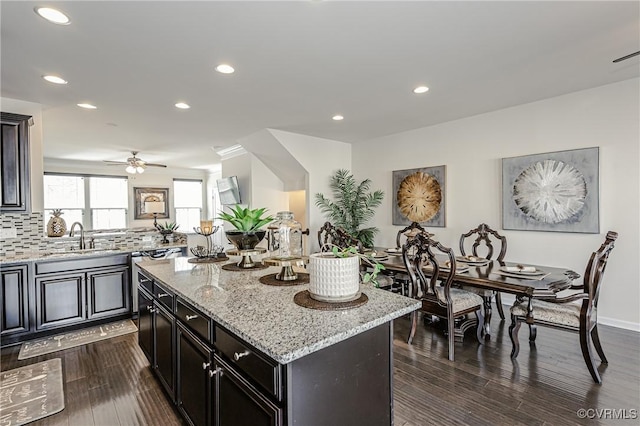 kitchen featuring light stone counters, dark wood-type flooring, a center island, a sink, and backsplash