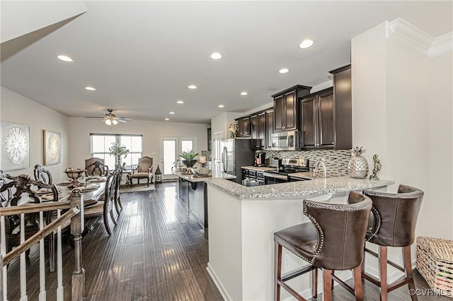 kitchen with decorative backsplash, light stone counters, a breakfast bar area, dark wood-style flooring, and stainless steel appliances