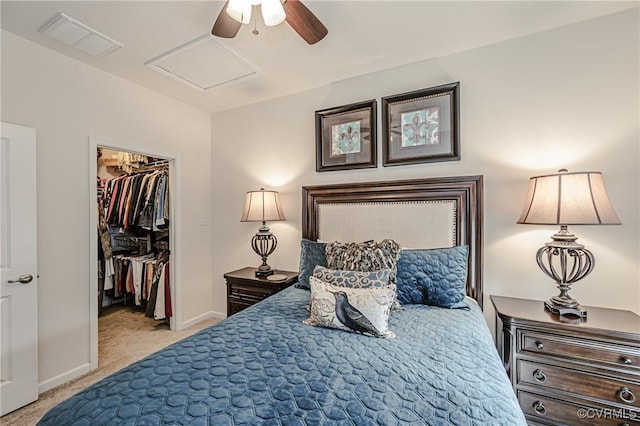 bedroom with a walk in closet, light colored carpet, visible vents, attic access, and baseboards