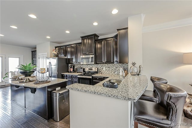 kitchen with decorative backsplash, a breakfast bar area, appliances with stainless steel finishes, light stone counters, and a sink