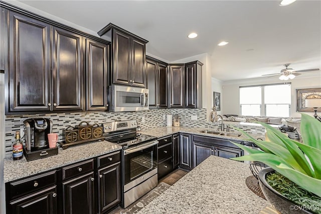 kitchen with a sink, open floor plan, appliances with stainless steel finishes, light stone countertops, and tasteful backsplash