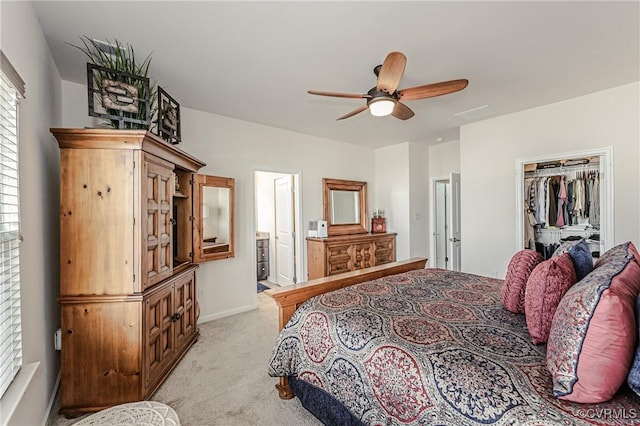 bedroom featuring a walk in closet, light colored carpet, ensuite bathroom, ceiling fan, and baseboards