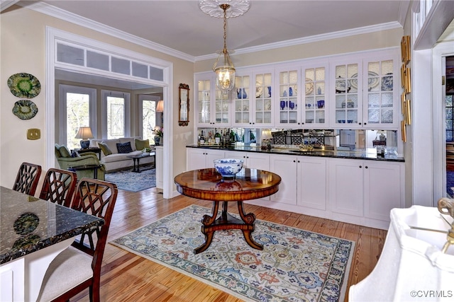 bar featuring light wood-style floors, crown molding, hanging light fixtures, and an inviting chandelier