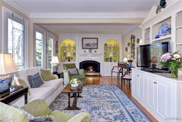 living room featuring built in shelves, a large fireplace, crown molding, and wood finished floors