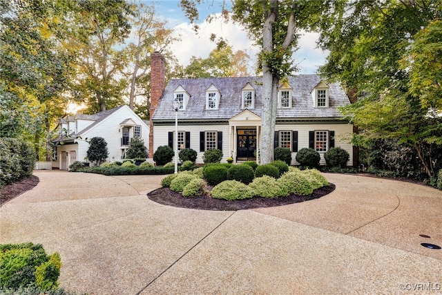 cape cod-style house featuring concrete driveway and a chimney