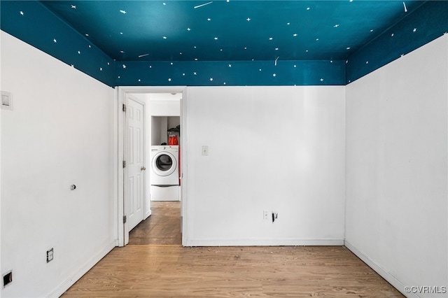 empty room with wood finished floors, washer / dryer, and baseboards