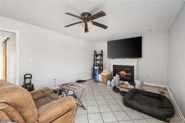 living room featuring light tile patterned flooring, a glass covered fireplace, a ceiling fan, and baseboards