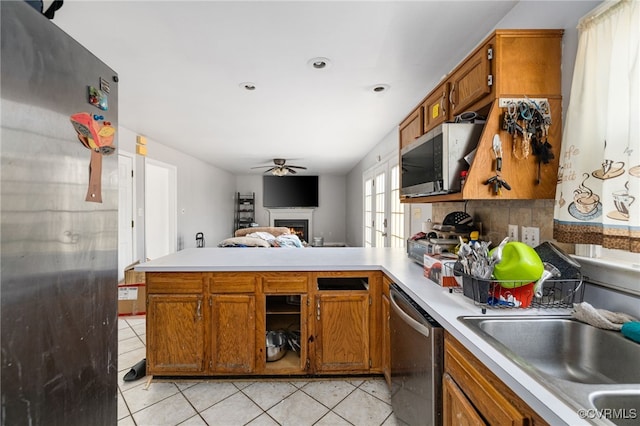 kitchen featuring light tile patterned flooring, a peninsula, light countertops, appliances with stainless steel finishes, and brown cabinetry