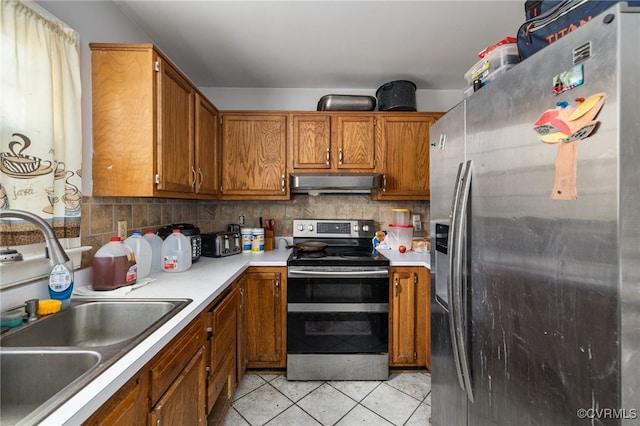 kitchen featuring light countertops, appliances with stainless steel finishes, brown cabinetry, a sink, and under cabinet range hood