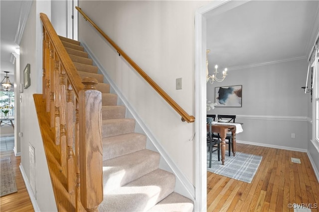 stairway with wood finished floors, crown molding, baseboards, and an inviting chandelier